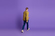 © deagreez - Young man in yellow plaid shirt walks away on purple background showcasing casual style lifestyle and fashion