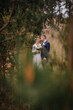 © Raivo - Couple in wedding attire stands together in a serene natural setting, surrounded by tall grass and trees, capturing a romantic moment in a beautiful outdoor environment