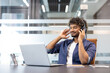 © Tetiana - Relaxed and smiling young Indian man in headphones sitting at his workplace in the office and listening to music