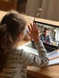 © Johannes - hispanic teen girl school college student distance learning waving hand studying with online teacher on laptop screen elearning zoom video call videoconference class with tutor over shoulder view no