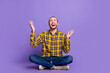 © deagreez - Young handsome guy checkered shirt sits cross legged on purple background smiling raising hands with joy energy lifestyle advertising fashion campaigns