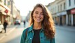 © miss irine - Young woman smiles brightly outdoors on city street. She wears teal denim jacket, black shirt. Sunlight illuminates her face and auburn hair. She looks happy and confident.