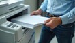 © miss irine - Man places stack of paper into office printer tray for scanning. Person uses modern copying machine for document work. Business task with tech equipment done indoors.