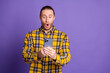 © deagreez - Young handsome man with smartphone surprised by screen wearing checkered yellow shirt against purple background