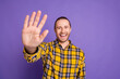 © deagreez - Young handsome guy in a yellow checkered shirt waves hello with smile in front of purple background lifestyle fashion advertising promotional imagery