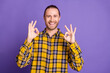 © deagreez - Young handsome guy in yellow plaid shirt smiles and makes ok gesture against purple background for fashion lifestyle advertising shopping concept