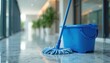 © miss irine - Blue mop and bucket rest on shiny marble floor hallway. Office building interior, plants line corridor. Cleanliness, janitorial service concept.