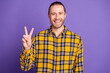 © deagreez - Young handsome guy in yellow checkered shirt smiles shows peace sign purple background casual model fashion advertising lifestyle stock imagery