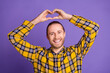 © deagreez - Young handsome man in yellow plaid shirt forms a heart with his hands against a purple backdrop for lifestyle and fashion stock image