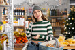 © JackF - Visiting store on New Years Eve, young woman is looking at something on shelf of showcase. She holds heavy basket of groceries and reaches for shelf, trying to see products in refrigerator window.