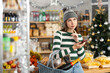 © JackF - Young woman in Santa hat are shopping on New Years Eve. In store near snack display case, she stand with phone, recall planned products, specify items according to notes.
