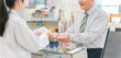 © buritora - A female pharmacist and an elderly man explaining medicines at the pharmacy register