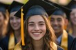 © Sean Hoong - A young woman wearing a black graduation cap and gown, standing in front of a group of similarly dressed graduates, with a backdrop of a large building and a clear blue sky.