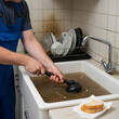 © Cliff - Plumber cleaning dirty clogged sink with plunger in kitchen. Close-up