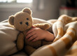 © Simon - - Child cuddling teddy bear in bed