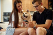 © standret - Guy is holding smartphone. Man and woman are sitting at home with Shibu Inu dog