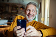 © Geber86 - Mature man happy and smiling while using smartphone at home