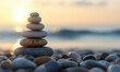 © Yuliia - Balanced stone stack on beach at sunset with blurred ocean background creating zen atmosphere for wellness and meditation.