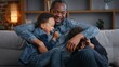 © Yuliia - Happy African American family fooling around playing on couch home father tickling two little children kids sons boys laughing play game joyful cuddling enjoying weekend tickle joy having fun positive