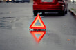 © Tricky Shark - Reflective emergency triangle stands behind disabled car on rainy urban road in the evening, road safety, driver caution, and correct procedure during an unexpected breakdown situation.