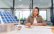 © PINA - female architect working on blueprint for house real estate project, asian woman engineer sitting in office planning on project alternative clean environment energy for sustainable business