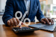 © Faiz - Businessman calculating interest rates using a calculator with a glowing percentage sign.