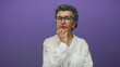 © Krakenimages.com - Woman with grey hair and glasses in white blouse thinking against a vibrant purple background, suggesting contemplation and wisdom in a modern studio setting.