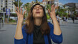 © Krakenimages.com - Hispanic woman in blue jacket and glasses raises hands on street under bright sunlight while frowning; frustration annoyance stress exasperation.