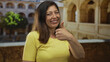 © Krakenimages.com - Woman in yellow shirt shows thumb up gesture in university building courtyard while smiling; approval.