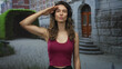© Krakenimages.com - Woman in maroon tank top with long wavy hair salutes on street by stone stairs with focused expression; pride.