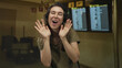 © Krakenimages.com - Woman cupping face with hands and smiling widely in busy airport terminal with departure signage overhead; travel excitement.