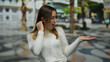 © Krakenimages.com - Woman smiling and pointing at an empty hand on a lively urban street backdrop, featuring a young blonde in a white sweater outdoors in broad daylight, full of vibrant charm.