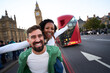 © CarlosBarquero - Joyful interracial couple having fun in London, with Big Ben and a red double decker bus behind. Playful piggyback pose, wide angle travel portrait that radiates energy and spontaneity.