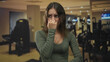 © Krakenimages.com - Woman pinching nose with hand and looking worried while standing in gym building near dumbbells and cardio machines; disgust unease.