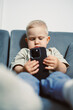 © DSMT - Focused young child engaged with smartphone while sitting on a cozy couch in a bright living room during the day