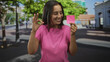 © Krakenimages.com - Young hispanic woman holding a pink sticky note with a drawn smiley and making an ok sign with her hand on a busy city street; happiness optimism.