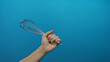 © Krakenimages.com - Caucasian man holding metal whisk isolated against blue wall background showcasing kitchen tool and cooking concept with simplicity and focus.
