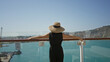 © Krakenimages.com - Woman raising arms overhead beside glass railing on cruise ship deck building under clear sky, wearing sunhat and black jumpsuit; serenity.
