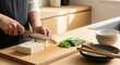 © Twenty One Studio - Person cutting tofu on a wooden cutting board in a kitchen.