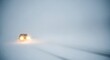 © Zumroatun - A car drives through a dense snowstorm, its headlights cutting through the whiteout conditions.