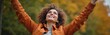 © Viktor - Young woman with curly hair raises arms up in celebration outdoors. She smiles looking up, feeling happy and free amidst autumn foliage. A joyful moment of personal triumph and optimism.