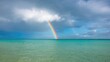 © vxnaghiyev - A vibrant rainbow arcs over a serene ocean, offering a colorful contrast to the white cloud, seasonal change
