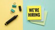 © SarminAkter - We're hiring' message on yellow sticky note with office supplies