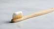 © Usman - Close up of a natural bamboo toothbrush with white toothpaste applied to the bristles on a light grey textured surface