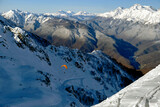 Beautiful, epic, stunning winter landscape of high mountains with bright yellow paraglider soaring above. Magnificent backdrop for extreme sports at the ski resort.