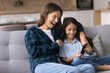 © fizkes - Laughing mom cuddle with tween girl on couch using phone