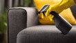 © Oleksandr - A hand in a yellow glove sprays cleaner onto a gray couch with a yellow pillow. Cleaning products for home care and a clean environment for healthier living indoors.