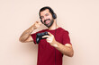© luismolinero - Man playing with a video game controller over isolated wall points finger at you while smiling