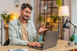 © Andrii Iemelianenko - Young man wearing headset, freelance worker, call center or support service operator helpline, talking with client or colleague communication support. Guy using laptop at home office desk. Lifestyle.