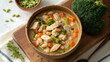 © MDRAHIMUL - A bowl of hearty chicken and vegetable soup with white beans, broccoli, and carrots, served on a wooden board with edamame and thyme, offering a comforting and nutritious meal